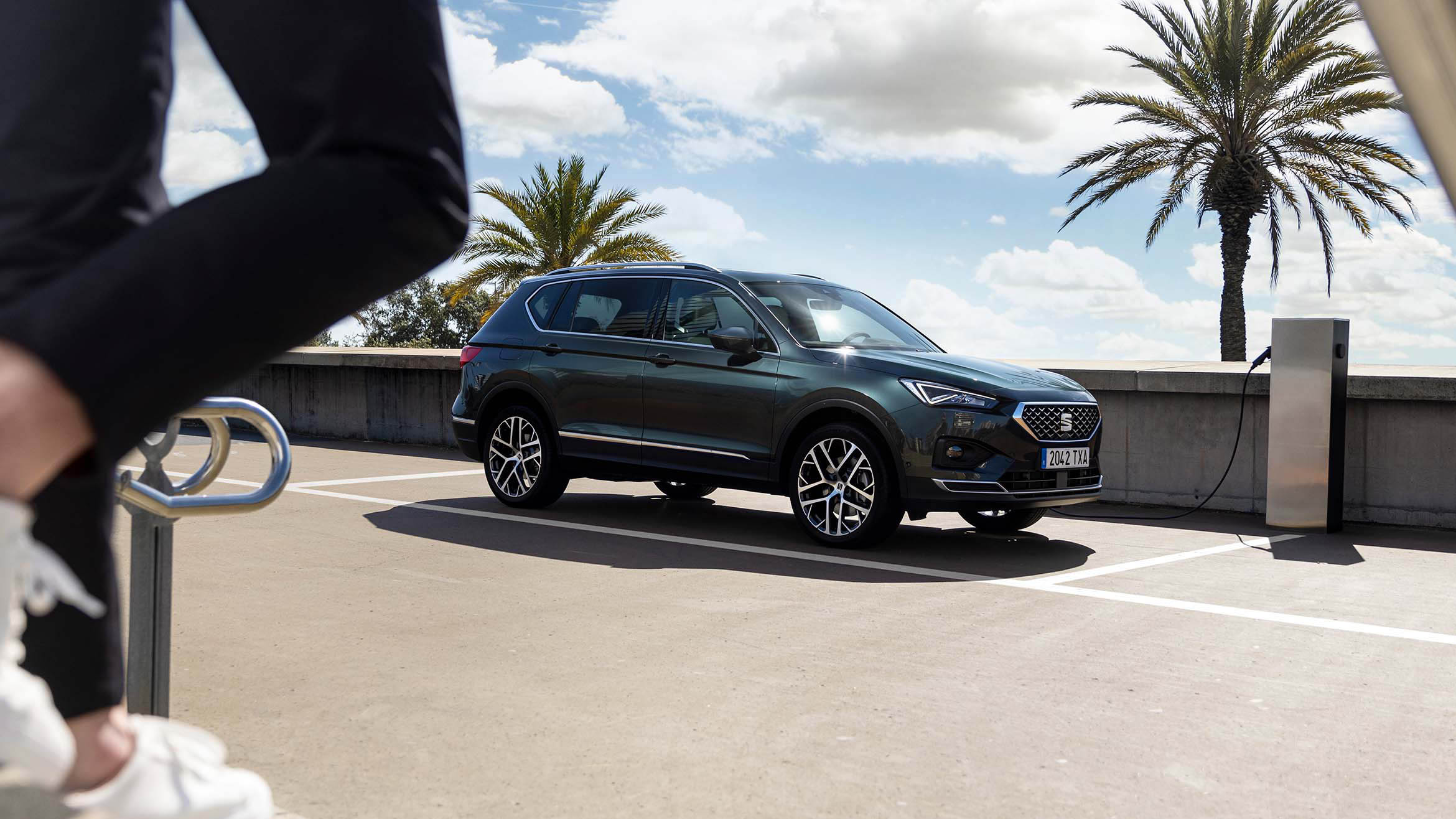 Link tamsiai žalios spalvos naujojo SEAT Tarraco XPERIENCE įkrovimo stotelėje eina žmogus